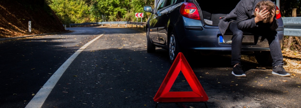Een man heeft pech met de auto en zit met zijn handen in het haar in de kofferbak
