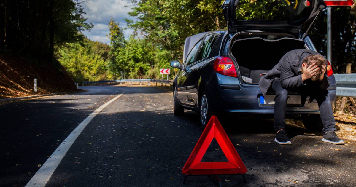 Een man heeft pech met de auto en zit met zijn handen in het haar in de kofferbak