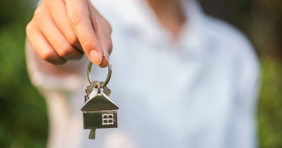 Een vrouw houdt de huissleutel vast met op de achtergrond groene bladeren