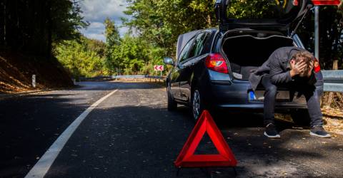 Een man heeft pech met de auto en zit met zijn handen in het haar in de kofferbak