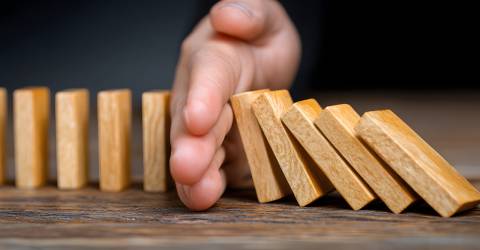 Een hand voorkomt een keting reactie van houten domino steentjes